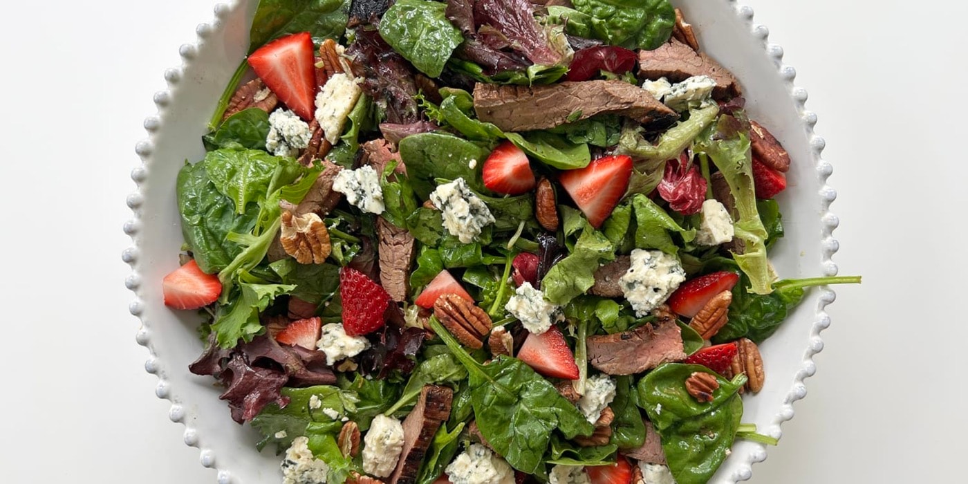 Sliced grilled steak over greens with strawberries and blue cheese